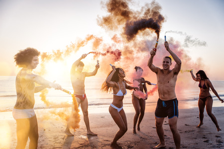 Group of friends having fun running on the beach with smoke bombsの写真素材