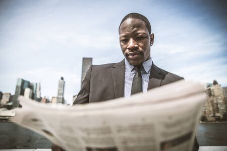 Confident businessman. Successful young man in full suit reading financial news on newspaper and drinking a cup of coffeeの写真素材