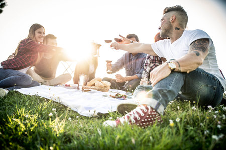 Group of friends having pic-nic in a park on a sunny day - People hanging out having fun while grilling and relaxingの写真素材