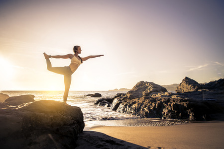 Woman training yoga on the beach at sunsetの写真素材
