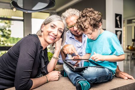 Grandchildren using digital tablet with their grandparents at home