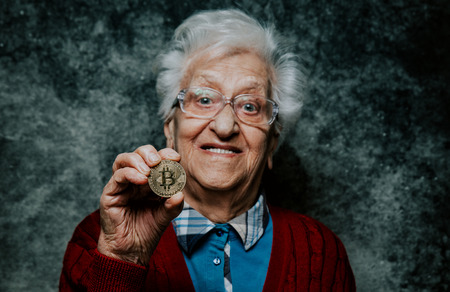 Old woman portrait holding a Cryptocurrency coinの写真素材