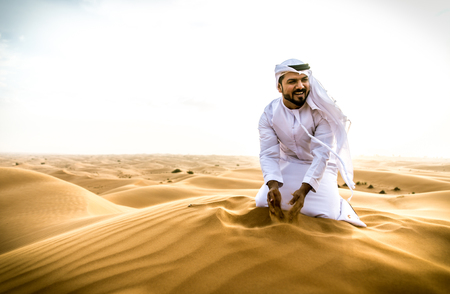 Arabic man with traditional emirates clothes walking in the desertの写真素材