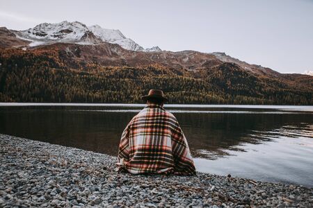 Lonely man enjoying sunrise on a lake beach with mountains backgroundの写真素材