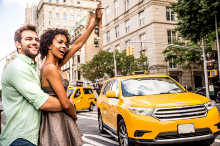 Interracial couple looking for a taxi in Manhattan - Tourists sightseeing New York on a yellow cabの写真素材