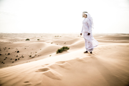 Arabic man with traditional emirates clothes walking in the desertの写真素材