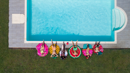 Happy people partying in an exclusive swimming pool with animal and fruit shapes mats, view from...