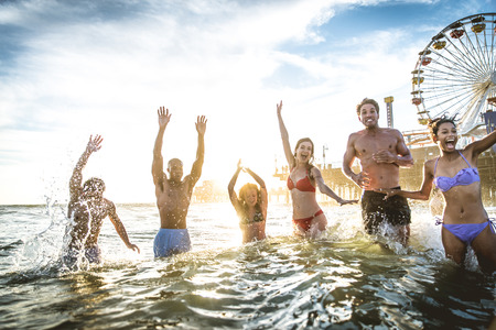 Group of friends splashing water while swimming in the sea - Multi-ethic group of people having fun on the beachの写真素材