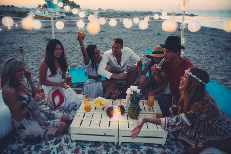 Group of friends making party on the beach at sunset time
