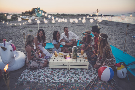 Group of friends making party on the beach at sunset time