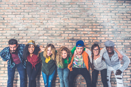 Group portrait of multi-ethnic boys and girls with colorful fashionable clothes holding friend in hands and posing on a brick wall - Urban style people having fun, studio shot - Concepts about youth  and togethernessの写真素材