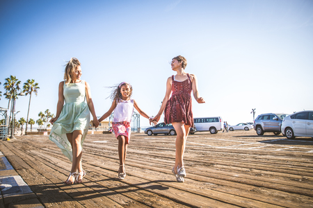Lesbians mothers with adopted child - Happy homosexual family playing with her daughterの写真素材