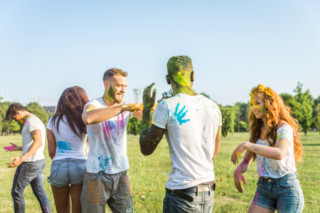 Group of happy friends playing with holi colors in a park - Young adults having fun at a holi...