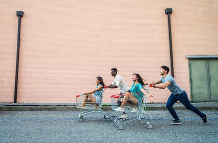 Multi-ethnic group of friends playing with shopping carts in a parkingの写真素材