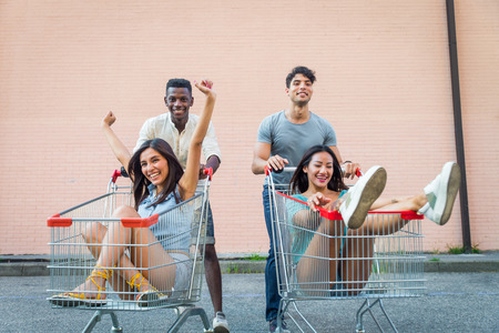 Multi-ethnic group of friends playing with shopping carts in a parkingの写真素材