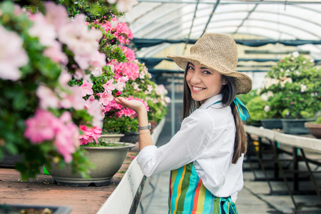 Pretty female gardener taking care of plants in her flowers and plants shop - Asian woman working in a greenhouseの写真素材