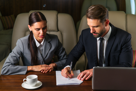 Businessman and woman working while travelling on private jet - Portrait of business people taking a first class flight for work, concepts about business and mobilityの写真素材