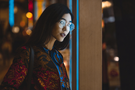 Beautiful mixed race woman posing outdoors, background with blurred neon lightsの写真素材