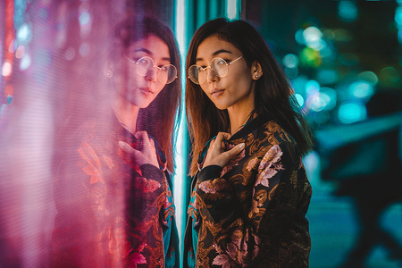 Beautiful mixed race woman posing outdoors, background with blurred neon lightsの写真素材