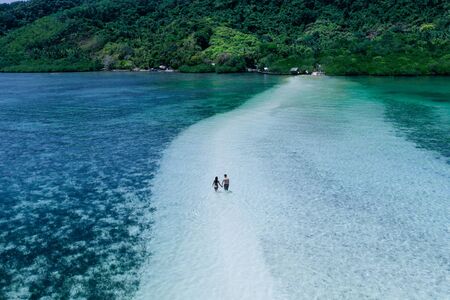 Enjoying the time at the beach. People walking on the white sand, with tropical jungle in the...