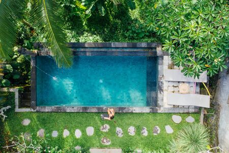 Beautiful girl relaxing outdoor in her garden with swimming pool. Summer concept about lifestyle,beauty, vacations and real estates. Aerial drone viewの写真素材