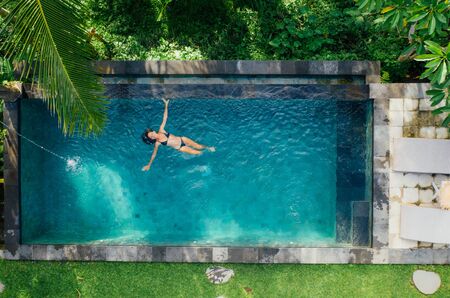 Beautiful girl relaxing outdoor in her garden with swimming pool. Summer concept about lifestyle,beauty, vacations and real estates. Aerial drone viewの写真素材
