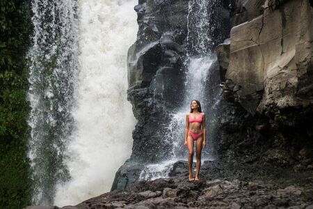 Beautiful young woman posing at the great Tegenungan waterfall in the deep rainforest of Bali island, Indonesia.の写真素材