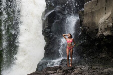 Beautiful young woman posing at the great Tegenungan waterfall in the deep rainforest of Bali island, Indonesia.の写真素材