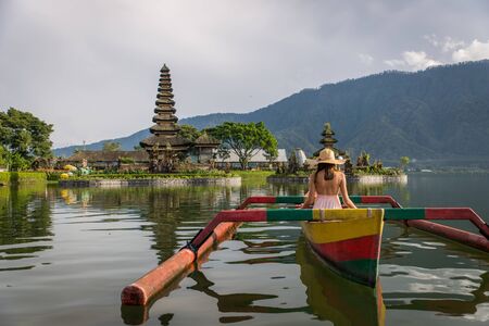 Young woman traveler paddling on a wooden boat at Pura Ulun Danu Bratan, Bali.の写真素材