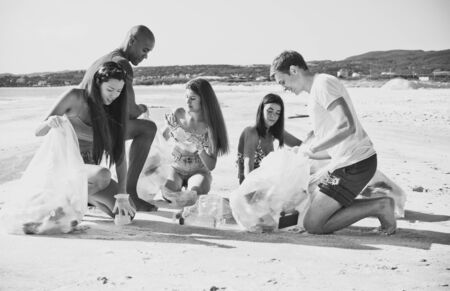 Group of activists friends collecting plastic waste on the beach. People cleaning the beach up, with...