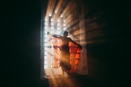 Children monk praying at the buddhist temple. artistic portrait with a monk silhouette in the mist and light filtering from a windowのeditorial素材