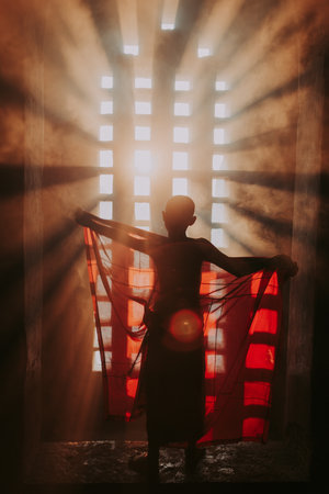 Children monk praying at the buddhist temple. artistic portrait with a monk silhouette in the mist and light filtering from a windowのeditorial素材