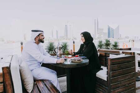 Happy couple spending time in Dubai. man and woman wearing traditional clothes having a conversation in a cafeの写真素材