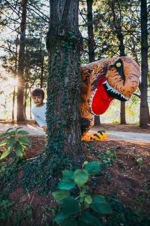 Father and son playing at the park, with a dinosaur costume, having fun with the family outdoorの写真素材
