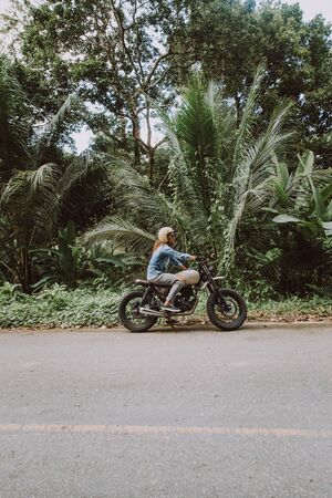 Beautiful girl having fun driving her custom cafe racer motorcycle, enjoying the sunset on the beachの写真素材