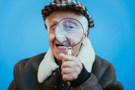 Funny portraits with old grandmother. Senior woman acting as an investigator with the magnifying...