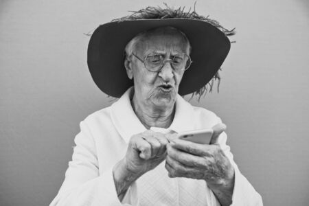 Funny grandmother portraits. Senior old woman, interacting with a smartphone. Concept about seniorityの写真素材