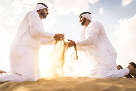 Arabian men with kandora walking in the desert - Portrait of two middle eastern adults with...