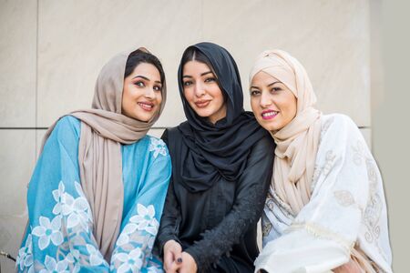 Arabic women with abaya bonding and having fun outdoors - Happy middleastern friends meeting and talking while shoppingの写真素材