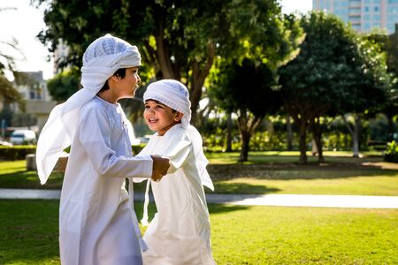 Group of middle-eastern kids wearing white kandora playing in a park in Dubai - Happy group of...