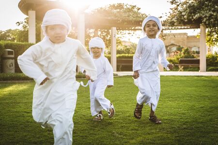 Group of middle-eastern kids wearing white kandora playing in a park in Dubai - Happy group of...