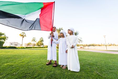 Group of middle-eastern kids wearing white kandora playing in a park in Dubai - Happy group of friends having fun outdoors in the UAEの写真素材