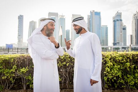 Two businessmen with traditional emirates clothes meeting in Dubai - Senior and young adults having...