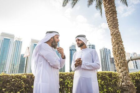 Two businessmen with traditional emirates clothes meeting in Dubai - Senior and young adults having...