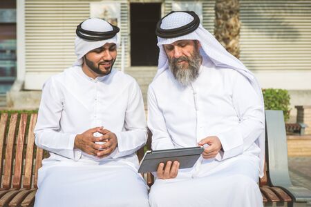 Two businessmen with traditional emirates clothes meeting in Dubai - Senior and young adults having business in the UAEの写真素材