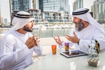 Two businessmen with traditional emirates clothes meeting in Dubai - Senior and young adults having business in the UAEの写真素材