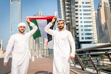 Middle-eastern young adults wearing kandora walking outdoors in Dubai - Two businessmen meeting...