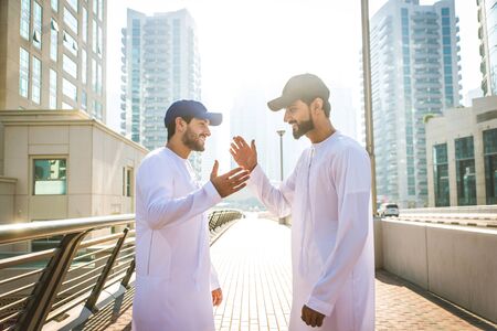Middle-eastern young adults wearing kandora walking outdoors in Dubai - Two businessmen meeting...