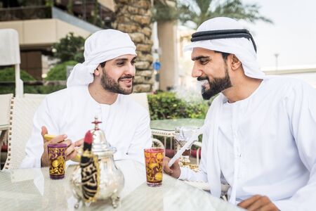 Middle-eastern young adults wearing kandora walking outdoors in Dubai - Two businessmen meeting...