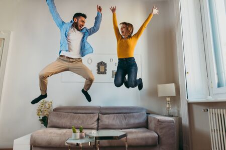 Young couple spending time together at home. Man and woman jumping on the couch and having funの写真素材